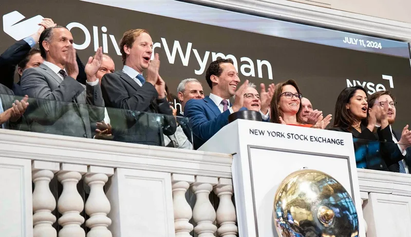 Oliver Wyman staff applauding at the bell podium of the New York Stock Exchange