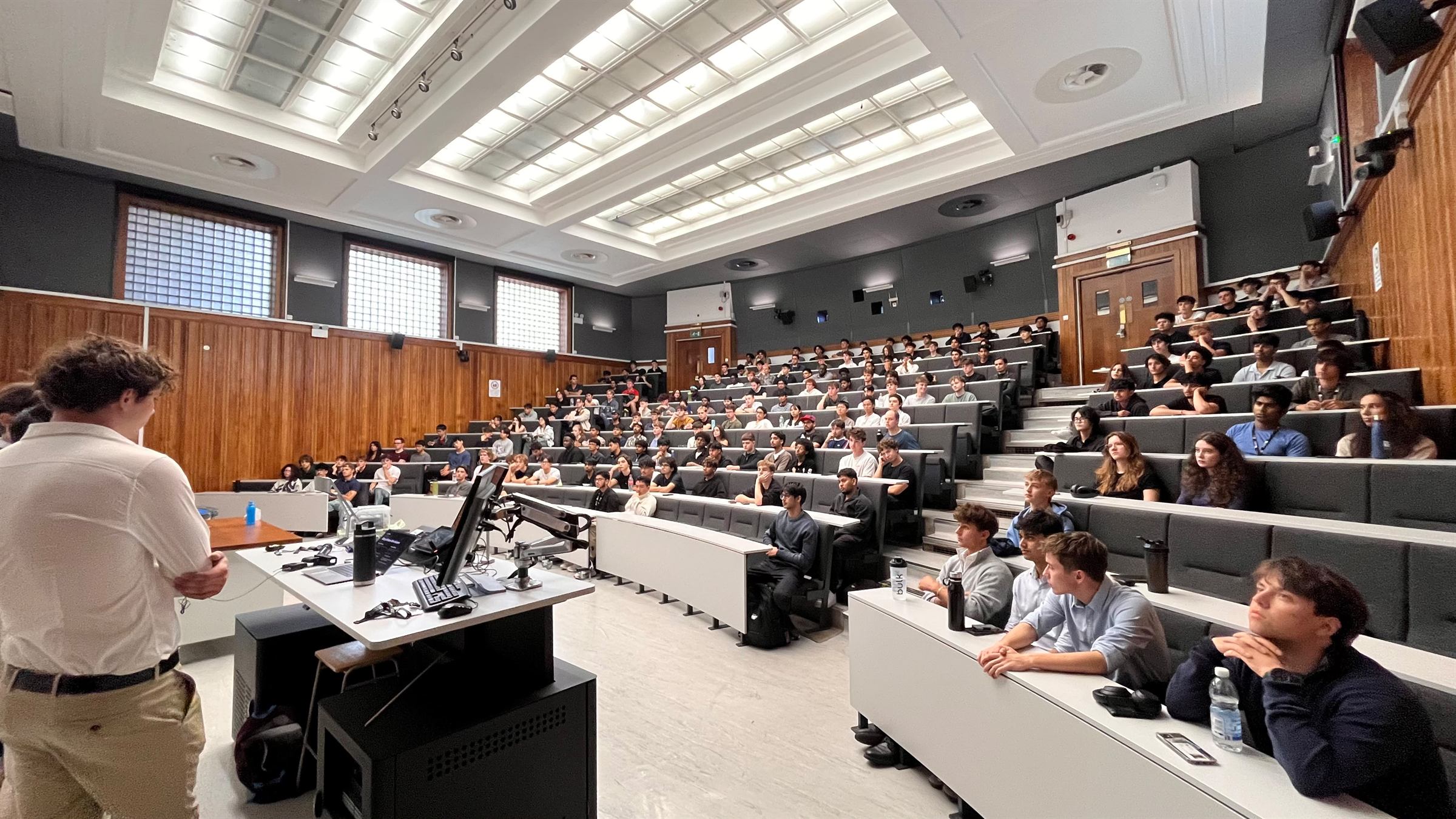 Pugsley Lecture Theatre filled to the back rows for the Bristol Trading Society Welcome Event, with a committee member presenting at the front.